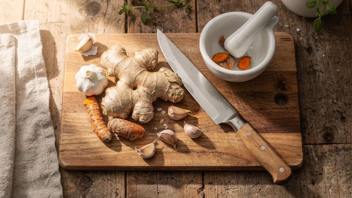 Ginger, turmeric, garlic, a knife, and a mortar and pestle on a wooden board