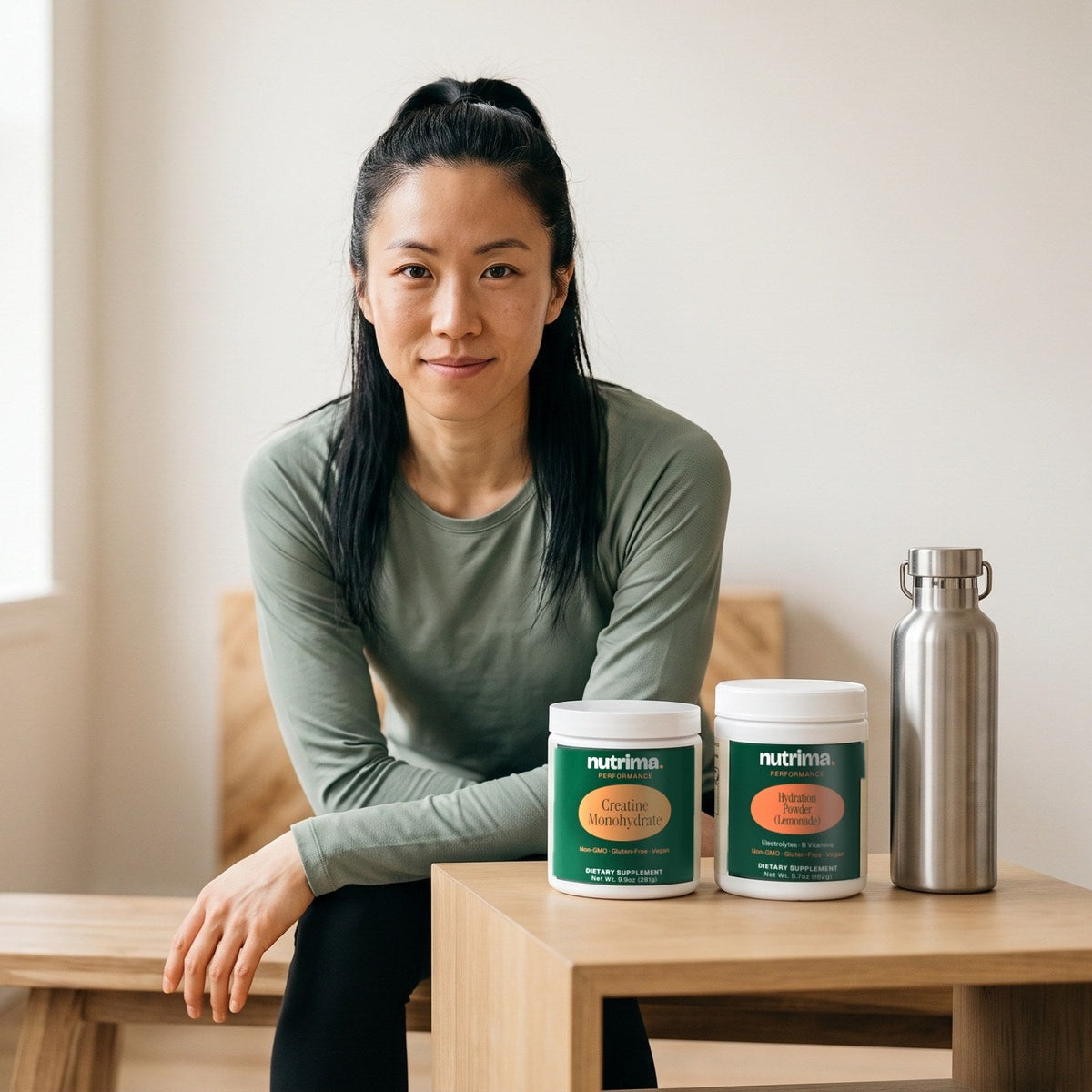 nutrima Performance collection: Creatine Monohydrate and Hydration Powder jars on a wooden table, a woman seated behind them — AI-generated brand image
