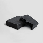 Two uneven pieces of Charcoal Soap showcasing a textured black surface, emphasizing its unique material, by nutrima.