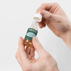 Hands opening a dropper bottle of Dark Spot Serum for Normal Skin by nutrima on a clean white background.