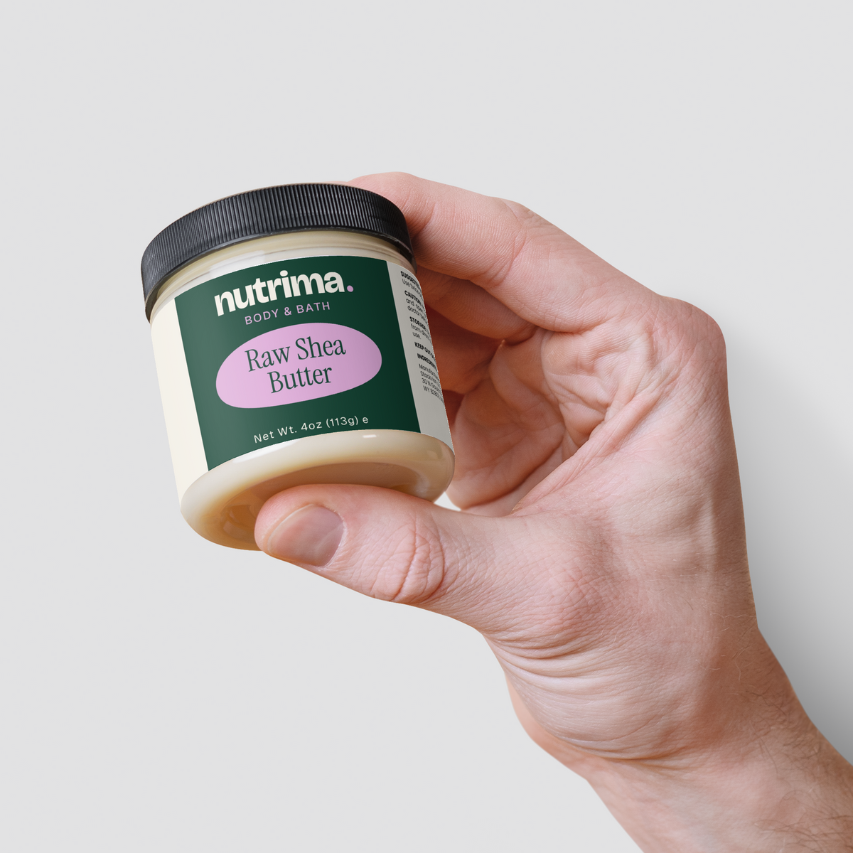 A hand holds a jar of Raw Shea Butter featuring a green and pink label, showcasing its 4 oz size by nutrima.