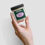Holding a jar of Raw Shea Butter with a distinctive label design by nutrima, showcasing its creamy texture and size.