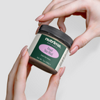 Hands holding a jar of Dead Sea Mud with a green label and pink accents, showcasing the product by nutrima.