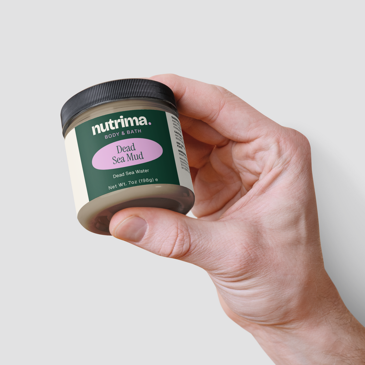 A hand holds a jar of Dead Sea Mud by nutrima, showcasing its distinct green packaging and label design.