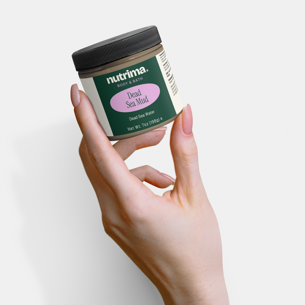 A hand holds a jar of Dead Sea Mud with a sleek design by nutrima, showcasing its green and pink label.