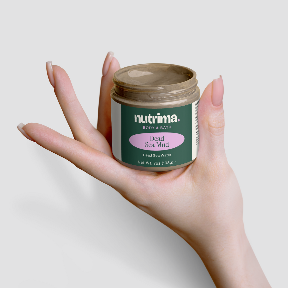 A hand holds a jar of Dead Sea Mud by nutrima, showcasing its unique packaging and earthy tone.