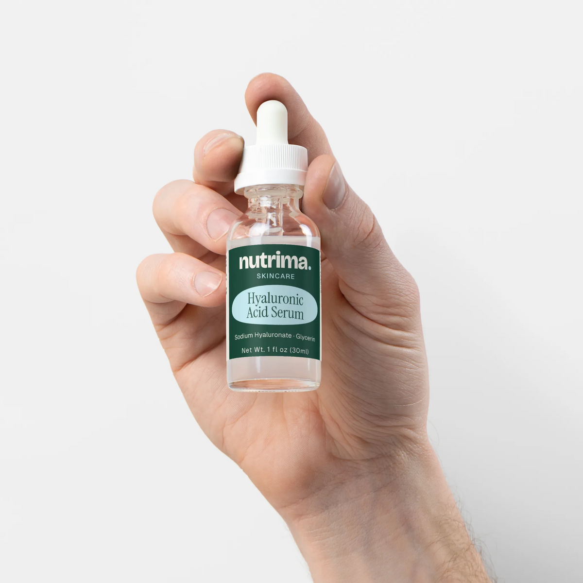 A hand holds a clear bottle of Hyaluronic Acid Serum with a dropper cap, featuring a teal label by nutrima.