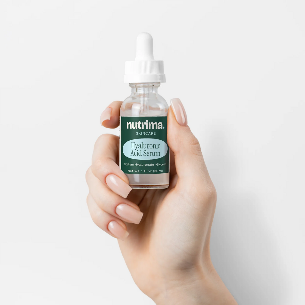 A hand holding a clear bottle of Hyaluronic Acid Serum showcasing the green label, by nutrima.