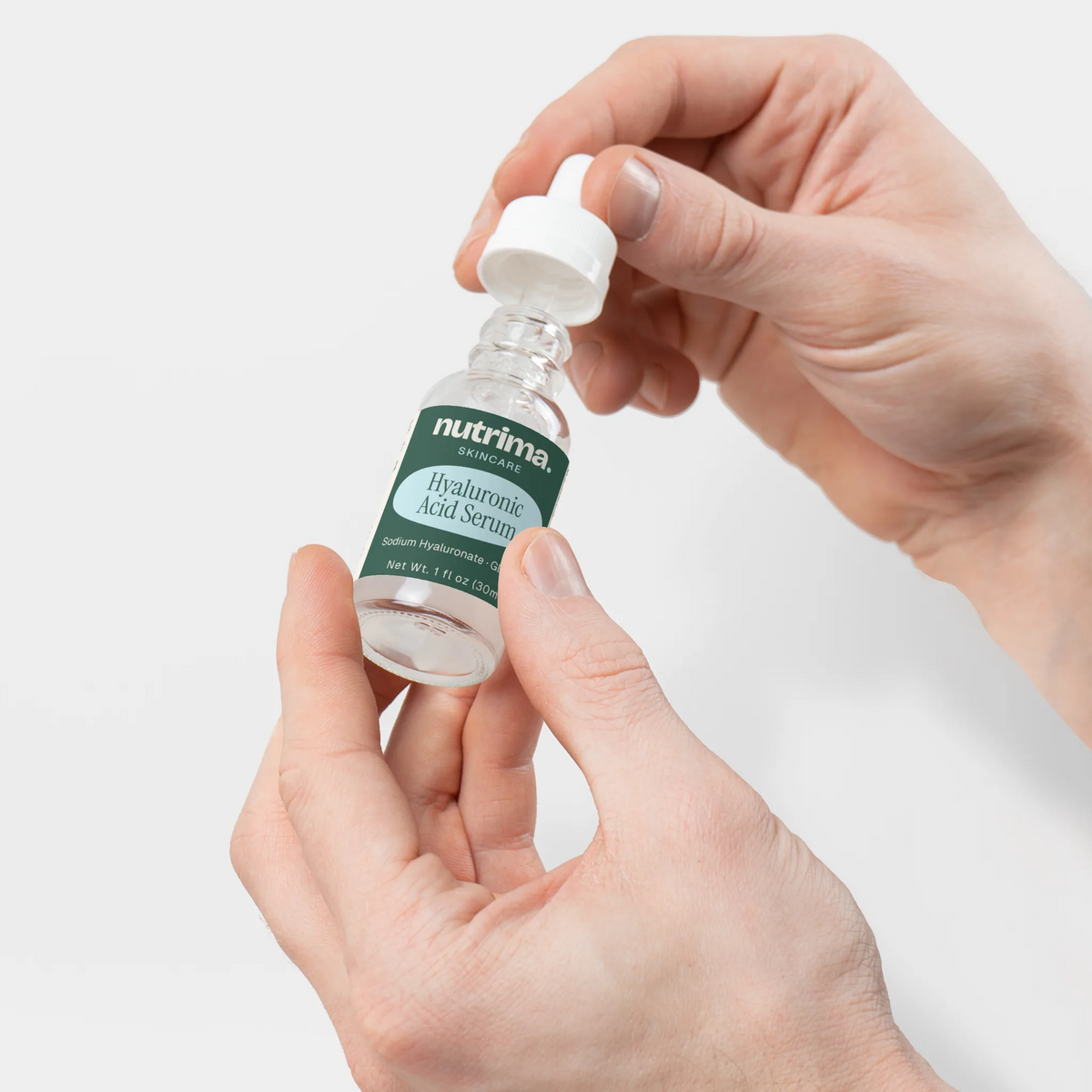 Hands holding a dropper bottle of Hyaluronic Acid Serum, showcasing the product's clear liquid and sleek design by nutrima.