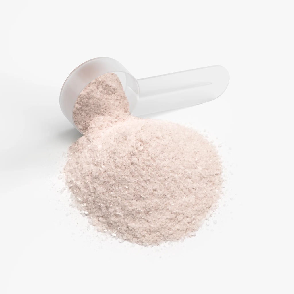 A scoop of pink Hydration Powder (Passion Fruit) spilling onto a white surface, showcasing its fine texture by nutrima.