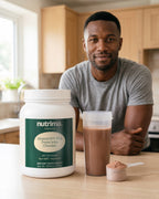 nutrima Advanced 100% Whey Protein Isolate (Chocolate) tub on a kitchen counter beside a shaker of chocolate shake, a man in the background — AI-generated brand image