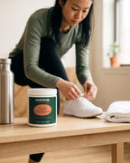 nutrima Creatine Monohydrate jar on a wooden bench beside a water bottle and towel, a woman tying her shoe in the background — AI-generated brand image