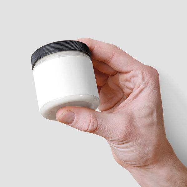 A hand holding a white jar of Recovery Cream with a black lid, designed by nutrima for body care.
