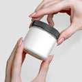 A person holding a white jar of Recovery Cream with a black lid, showcasing its sleek design by nutrima.
